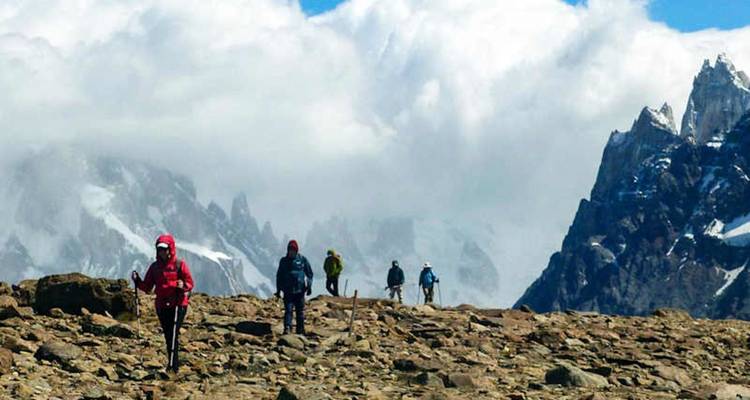 Les randonneurs traversent un plateau rocheux en direction de pics de granit enneigés qui percent les nuages tourbillonnants.