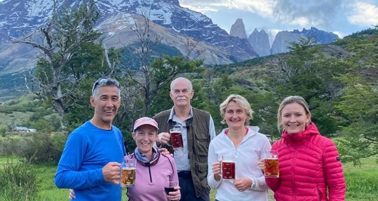 Cinq randonneurs trinquent avec des chopes de bière sous des pics montagneux escarpés et des vallées verdoyantes.