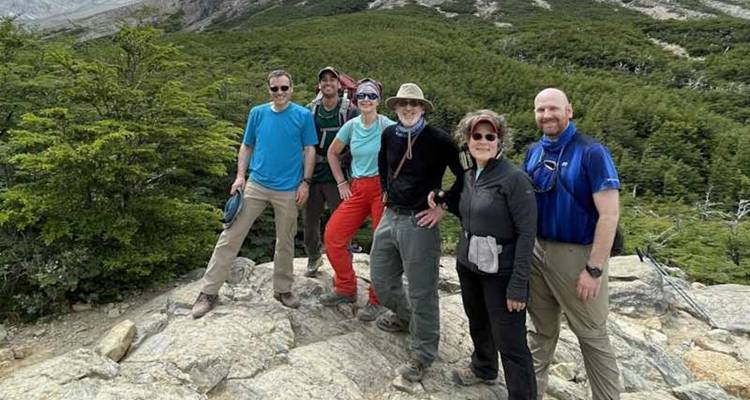 Un pequeño grupo de senderismo está parado en un afloramiento rocoso sobre un denso bosque verde en la Patagonia.