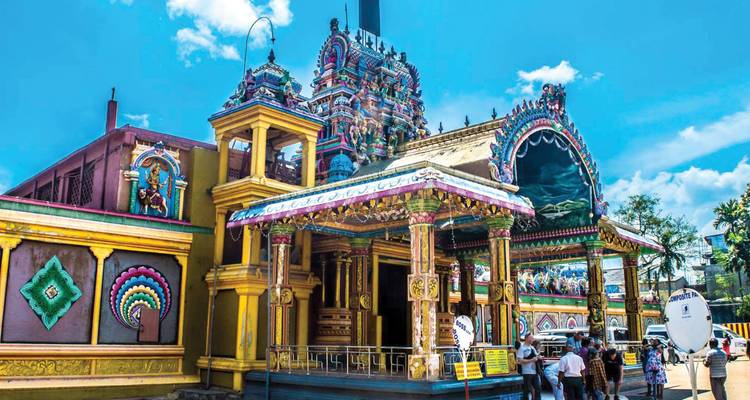 Lebendiger hinduistischer Tempel mit verzierter, farbenfroher Fassade und Besuchern in der Nähe.