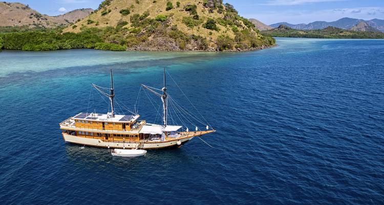Classic phinisi yacht anchored in calm turquoise bay backed by green hills