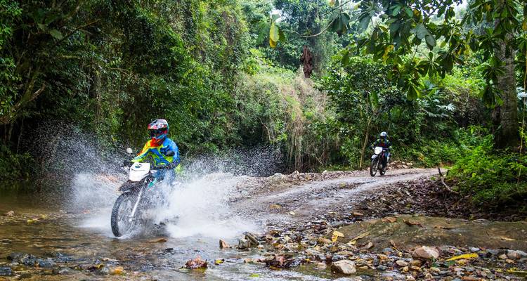 Les motocyclistes éclaboussent à travers un ruisseau peu profond sur une piste forestière.