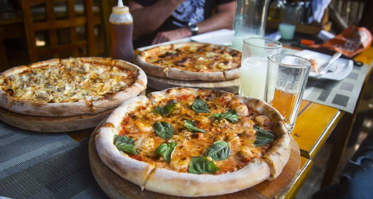 Trois planches en bois supportent des pizzas fraîches et des boissons sur une table de restaurant.