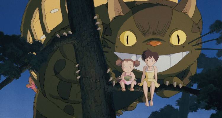Animated scene of two young girls sitting on a tree branch beside a large smiling cat-bus character, set at dusk with deep blue sky behind.