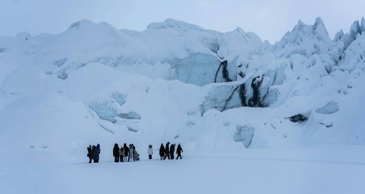 Guided group stands dwarfed by towering blue ice cliffs on a snowfield during a glacier hike.