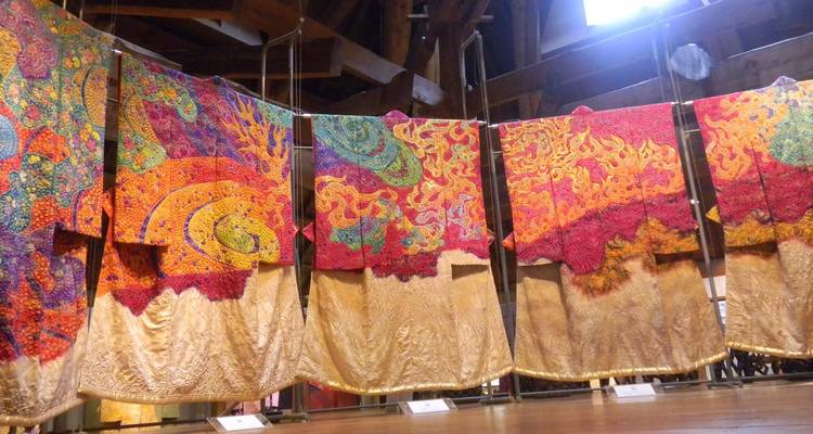 Vibrant kimonos with intricate patterns hang on display inside a traditional workshop.