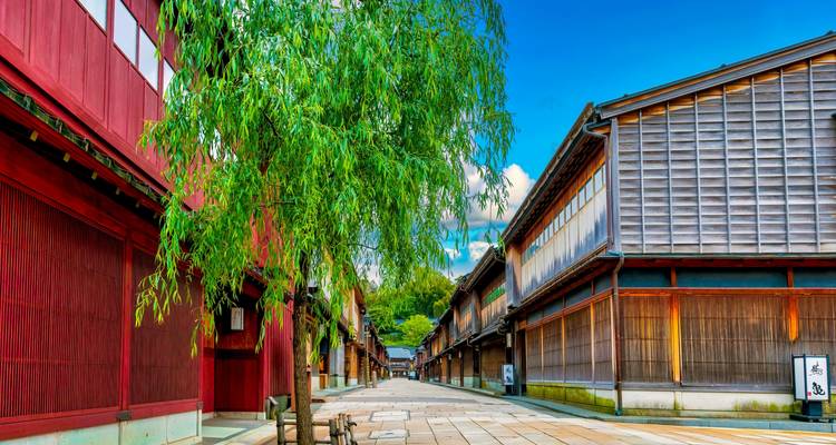 Traditional wooden machiya line a stone street under a bright blue sky in Kanazawa’s preserved district.