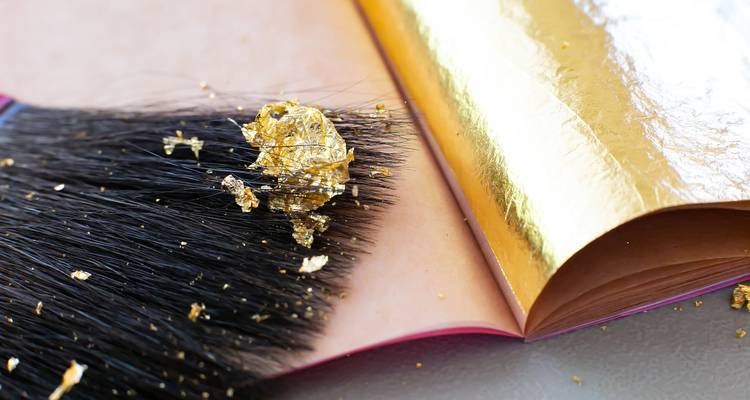 Close-up of a brush and delicate gold leaf sheets used in traditional gilding.