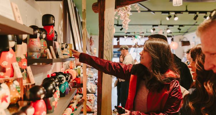 Shoppers browse wooden kokeshi dolls in a cozy Japanese craft store.