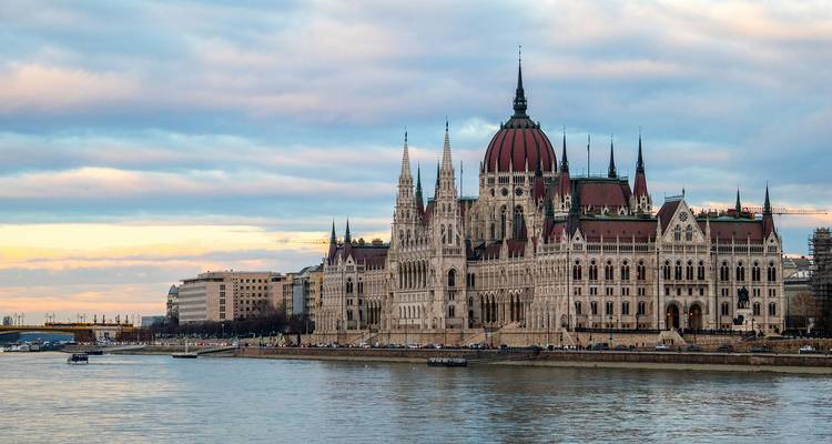 Le bâtiment emblématique du Parlement hongrois se reflétant dans le Danube sous un ciel de coucher de soleil aux teintes pastel.
