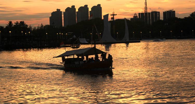 Bateau en silhouette sur la baie de Jakarta au coucher de soleil spectaculaire avec la skyline de la ville en arrière-plan