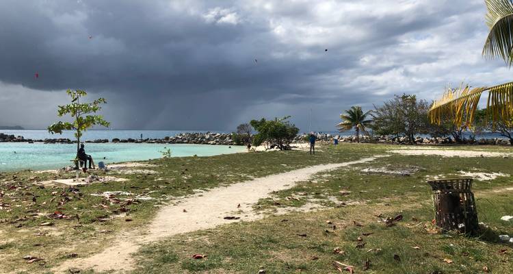 Ciel orageux surplombant une petite péninsule avec des palmiers et des eaux peu profondes turquoise