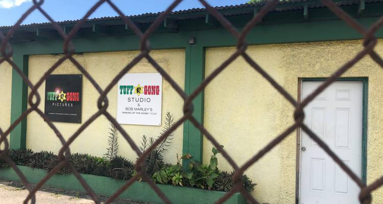 Vue de l'enseigne du studio Tuff Gong partiellement obscurcie par une clôture à mailles losangées