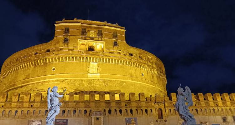Castel Sant'Angelo illuminated in golden tones with angel statues in foreground at night