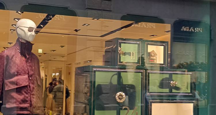 Luxury Prada storefront display with mannequin and green cabinetry behind reflective glass
