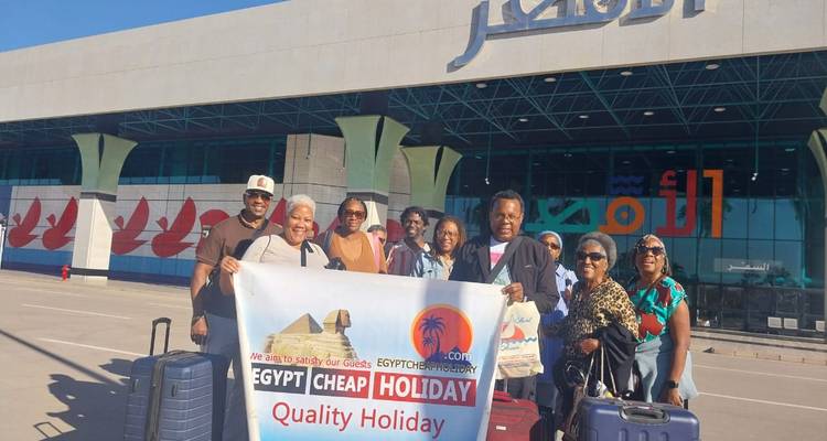 A group with suitcases smile outside Luxor airport holding a banner for their Egyptian holiday.