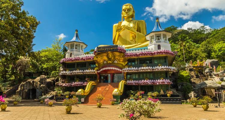 The colorful Golden Temple of Dambulla, crowned by a giant gold Buddha, gleams under a blue sky.