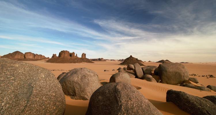Rounded granite boulders rise from orange Sahara sand beneath a crisp blue sky.