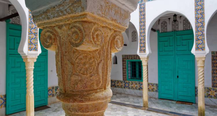 Ornate stone column and turquoise doors in a traditional Algerian courtyard.