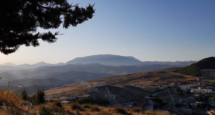 Late-afternoon light washes over rolling hills and a mountain backdrop with a small town below.