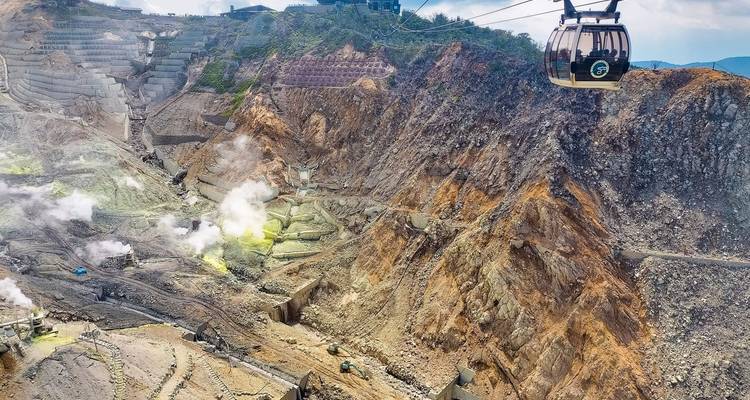Aerial view of Owakudani volcanic valley with rising steam and ropeway cabin passing overhead.