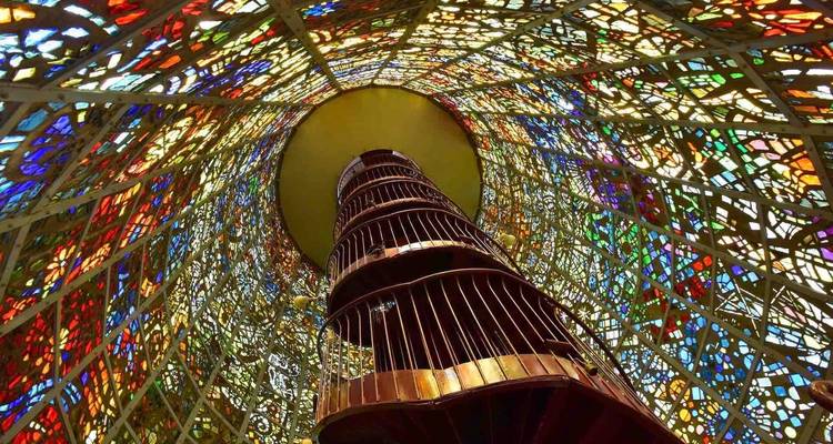 Looking up a spiral staircase encased in vivid multicolored stained glass panels.