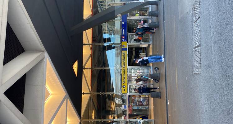 Straatgezicht van de moderne glazen ingang van Napoli Stazione Garibaldi met reizigers buiten.
