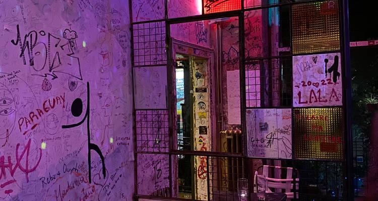 Dimly-lit interior of a graffiti-covered ruin pub with colorful neon lighting and mirrors