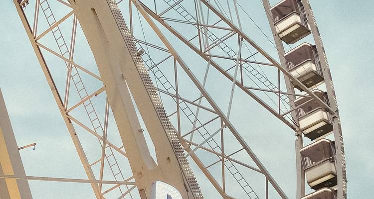 Close-up of a modern Ferris wheel’s white metal structure against a light blue sky