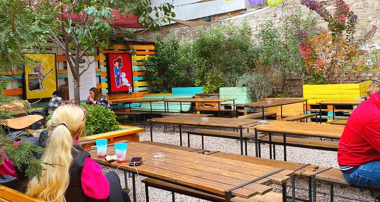 Colorful outdoor beer-garden courtyard with wooden benches, plants and a few patrons