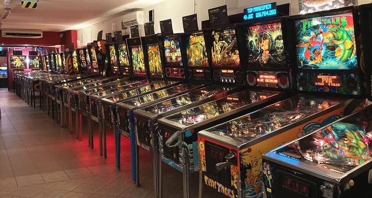 Long row of brightly lit vintage pinball machines inside an arcade hall