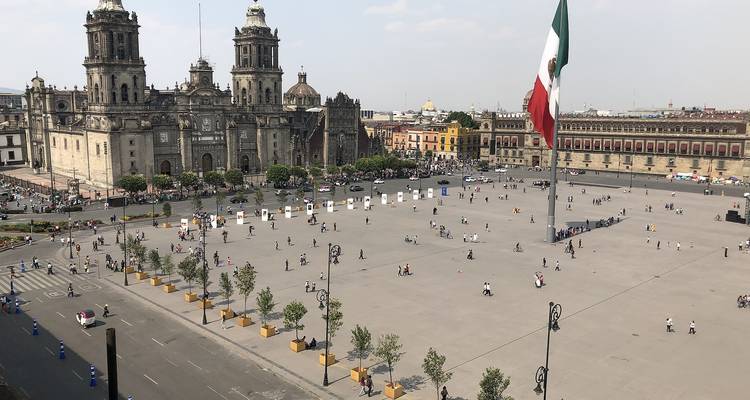 Wide aerial view of Mexico City's Zócalo with the giant national flag and Metropolitan Cathedral dominating the historic square.