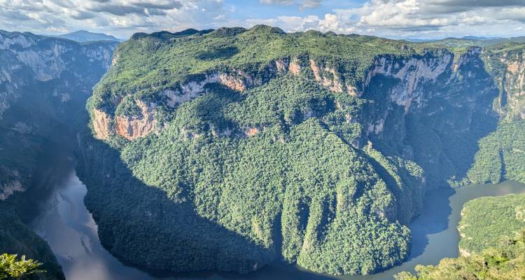 Bright panoramic shot of a massive verdant cliff peninsula surrounded by a serpentine river deep in a canyon.