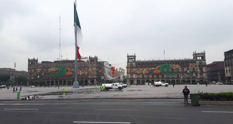 Mexico City's main square decorated with colorful patriotic light displays across the government buildings on an overcast morning.