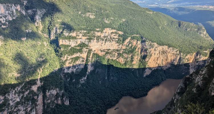 Steep rock walls cast shadows over a muddy river far below a canyon lookout point.