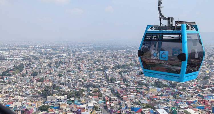 Blue panoramic gondola of the Cablebús glides high above the sprawling urban landscape of Mexico City.