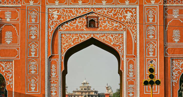 Una ornada puerta de ciudad naranja en Jaipur enmarca un palacio distante, con un semáforo al frente.