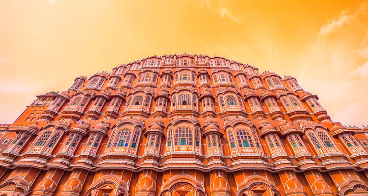 Vista ascendente de las ventanas de panal de abeja del Hawa Mahal brillando bajo un cielo naranja.