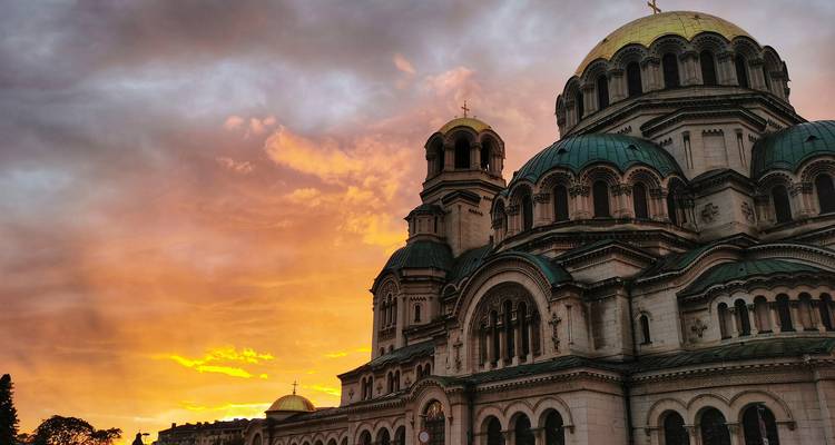De koepels van de Alexander Nevsky Kathedraal steken af tegen een vurig oranje zonsonderganghemel in Sofia.
