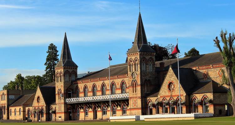 Rotes Backsteingebäude aus der viktorianischen Ära mit spitzen Türmen und dekorativen Bögen vor klarem blauen Himmel.