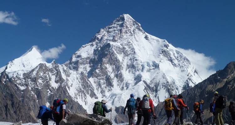 Les randonneurs s'approchent d'un pic massif couvert de neige qui s'élève brusquement contre un ciel bleu profond.