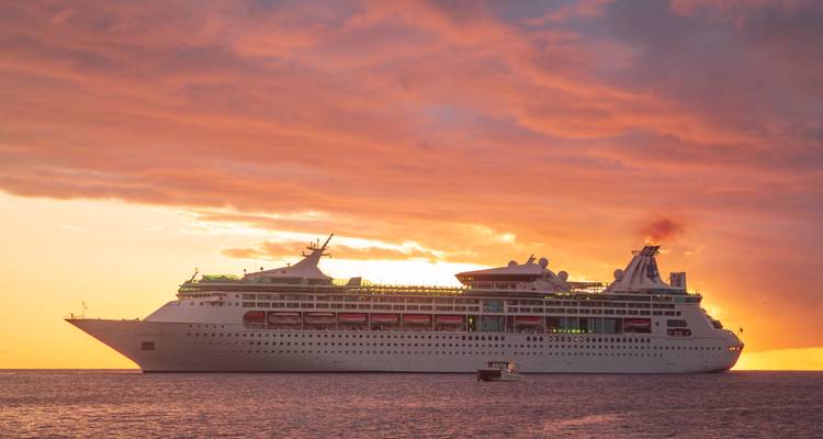 Large white cruise ship at sea silhouetted against a colourful sunset sky.