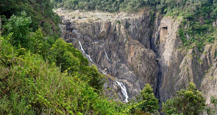 Rugged gorge with multiple small waterfalls plunging over rocky cliffs surrounded by forest.