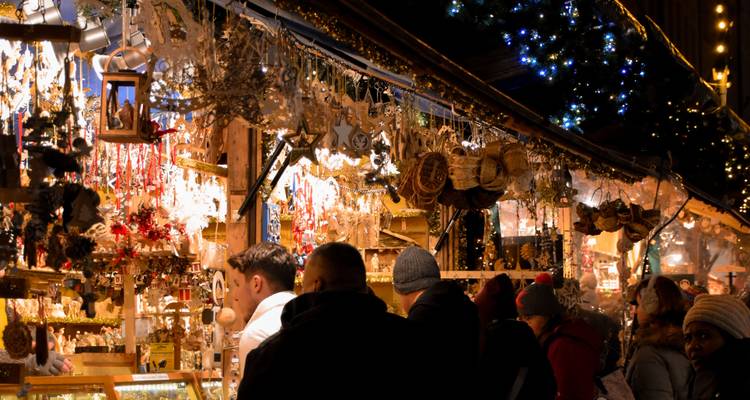 La gente pasea entre adornos hechos a mano en un mercadillo navideño al aire libre, iluminado con calidez, durante la noche.