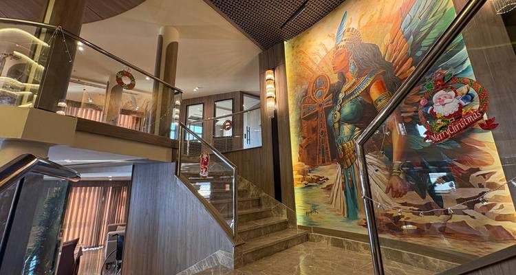 Vestíbulo del barco con escaleras de mármol y un gran mural colorido de una reina egipcia, decorado para Navidad.
