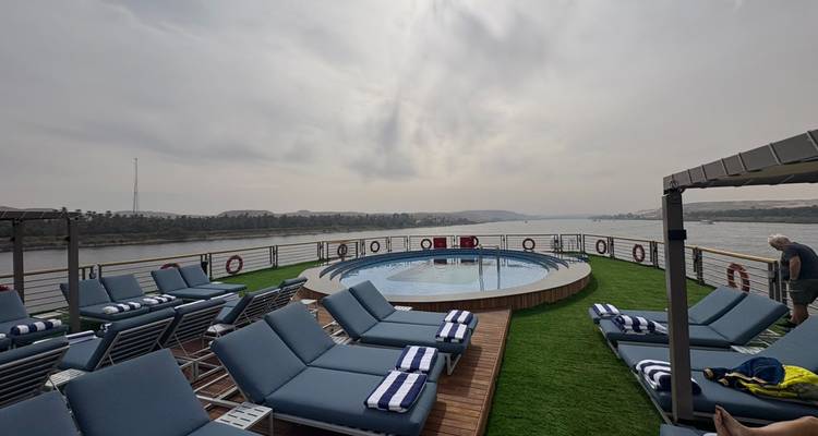 Piscina en la cubierta superior con tumbonas con vista al Nilo, algunos viajeros relajándose cerca de la barandilla.