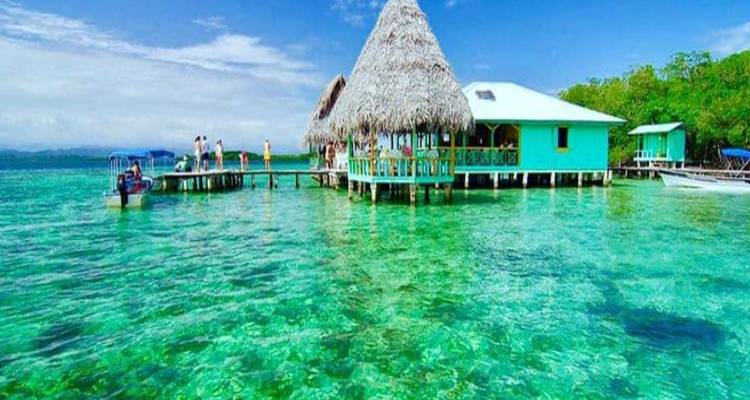 L'eau cristalline des Caraïbes et les huttes au toit de chaume sur pilotis dans un resort flottant animé.