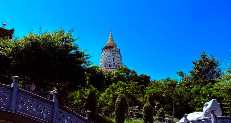La haute pagode dorée de Kek Lok Si s'élève au-dessus d'une verdoyante colline et d'escaliers en pierre sous un ciel bleu éclatant.
