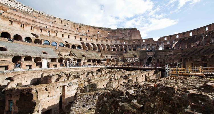 Wide interior of the Colosseum lit by sunlight with restored walkways and exposed subterranean chambers.