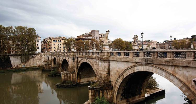 Stone arches of Ponte Sant’Angelo span the calm Tiber River with reflections of Rome’s muted skyline.